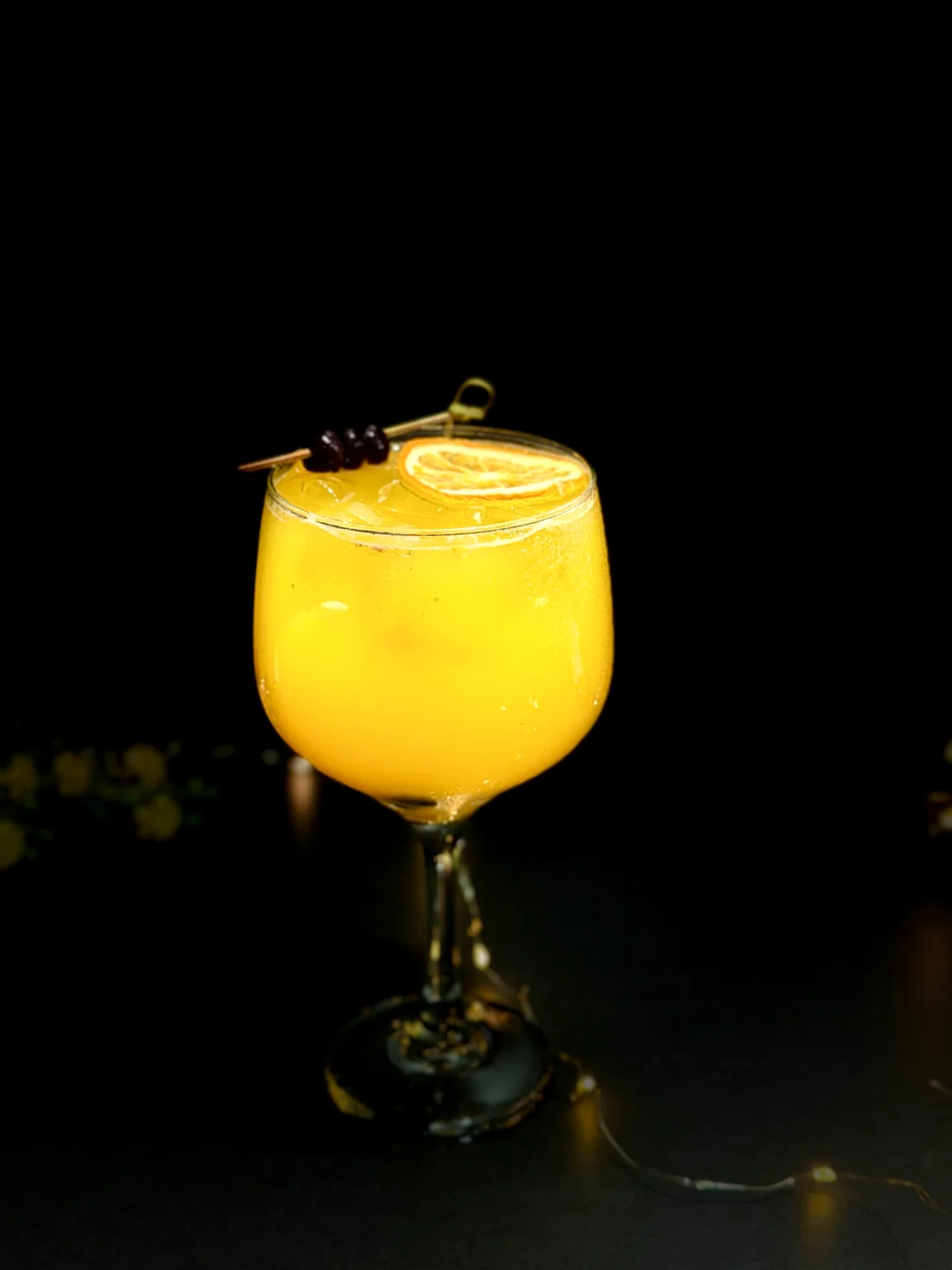Cóctel amarillo sobre fondo negro con naranja deshidratada