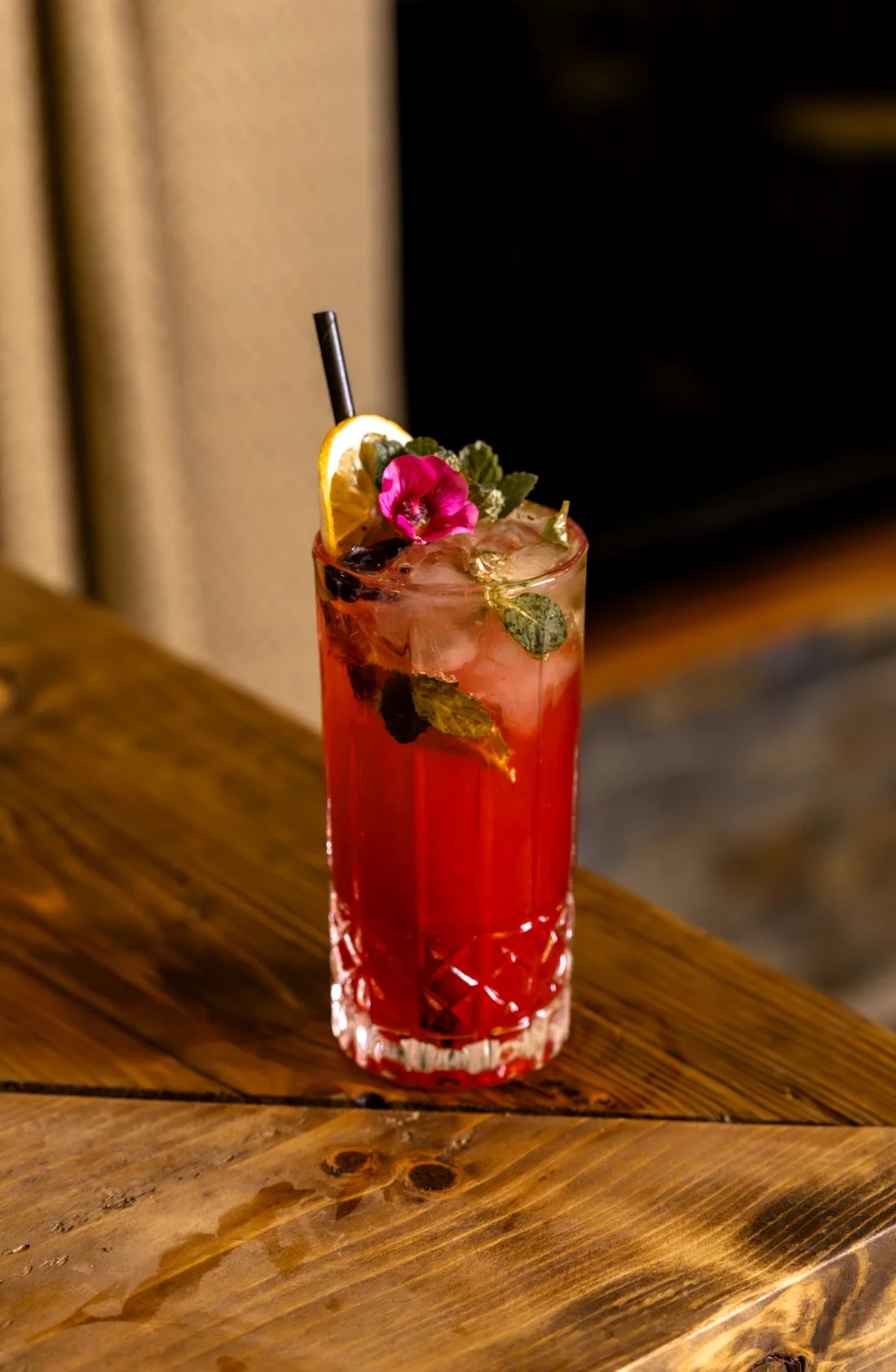 Cóctel rojo con hielo, menta, cítrico y flor comestible